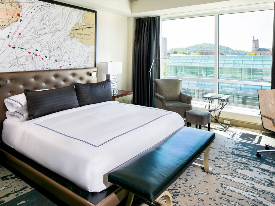 Quarto de hotel com uma cama grande, uma escrivaninha, uma cadeira e vista para a cidade.
