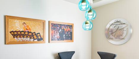 A dining area with a round glass table and four chairs, framed artwork on the walls, and a decorative light fixture.
