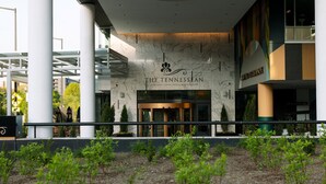 A modern hotel entrance with a marble facade, a large circular light fixture, and a sign reading "The Tennessean Personal Luxury Hotel Residences".