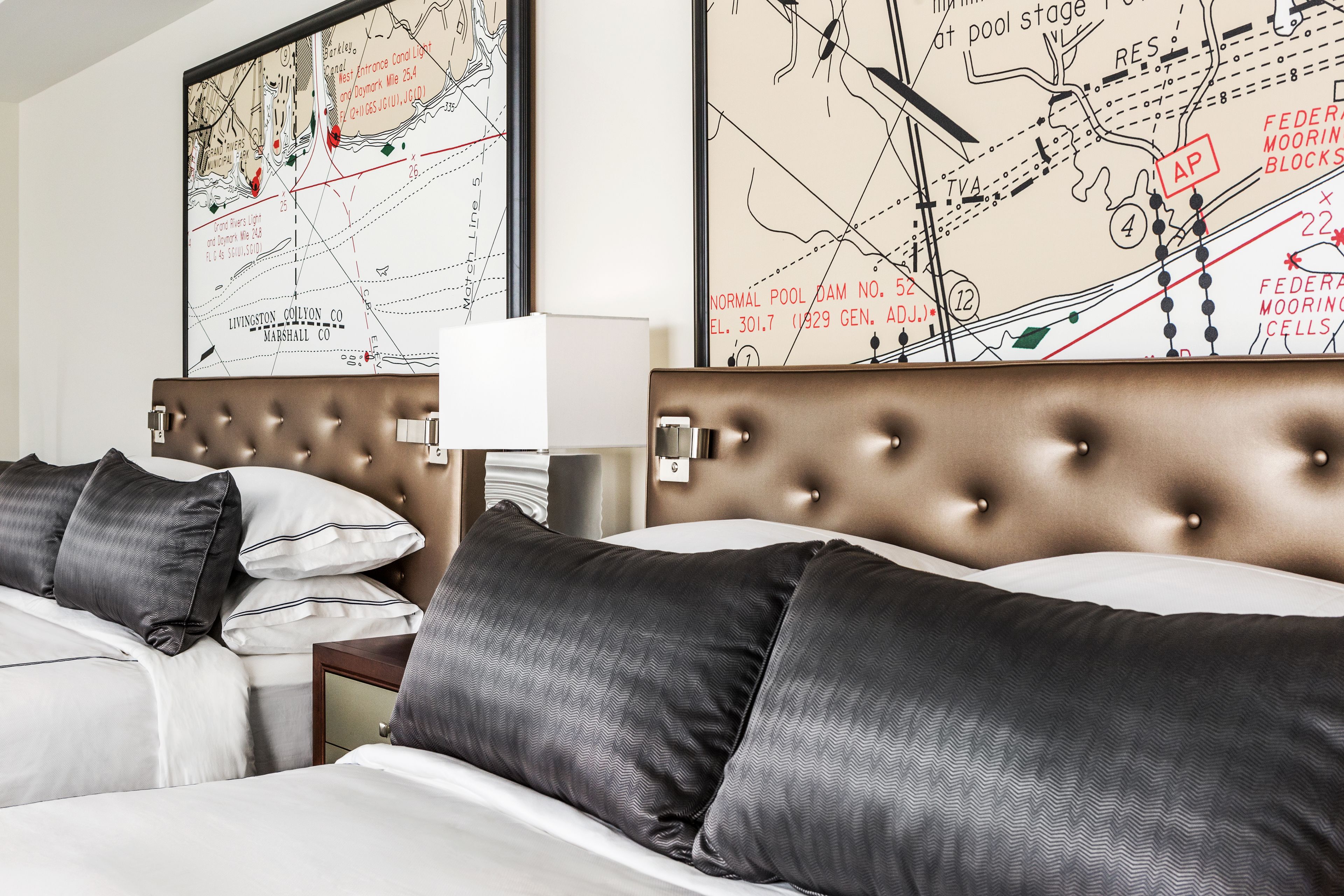 A hotel room with a large bed, two nightstands, a lamp, and two large maps on the wall.