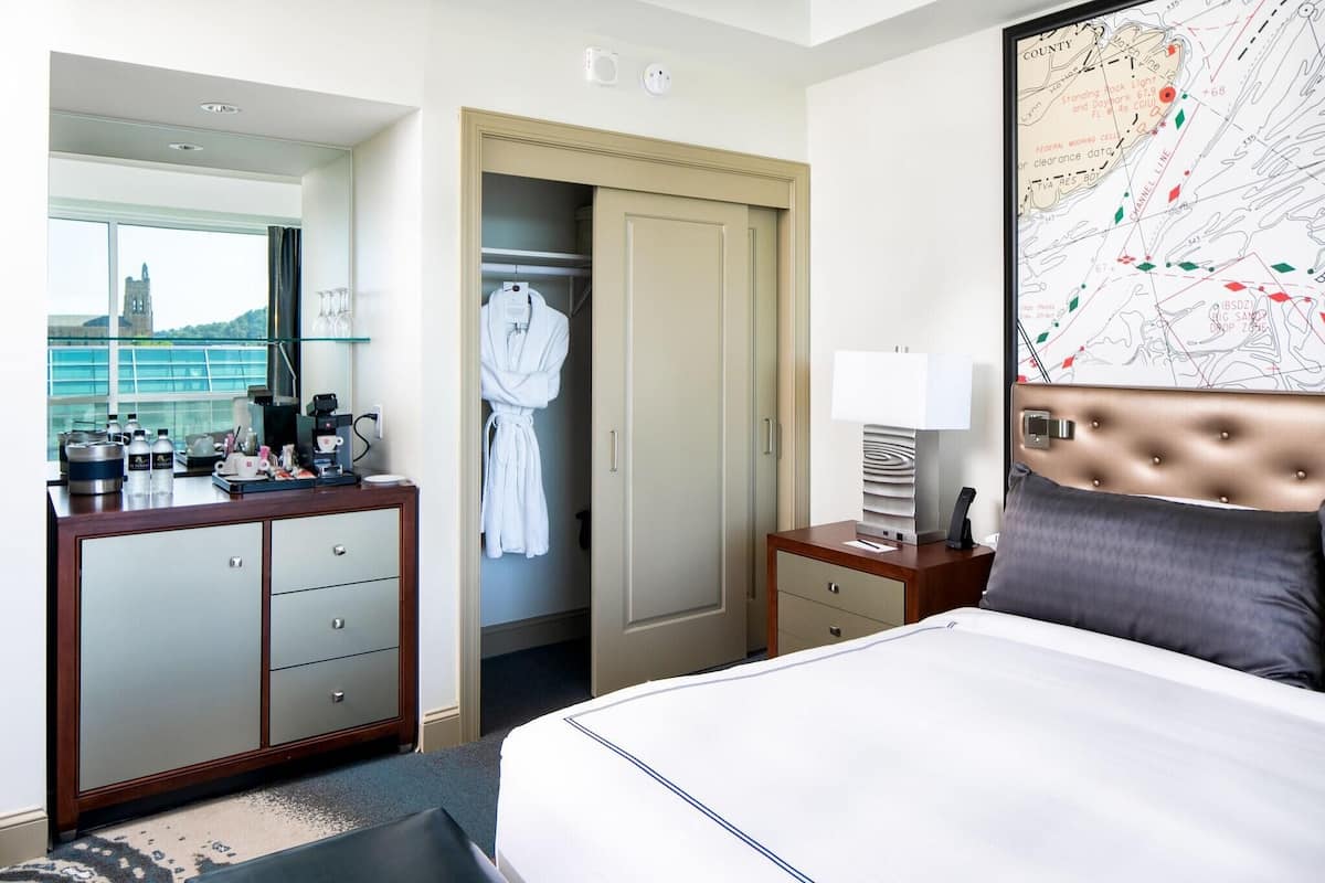A hotel room with a bed, a dresser, a closet, a map on the wall, and a window with a view of a building.
