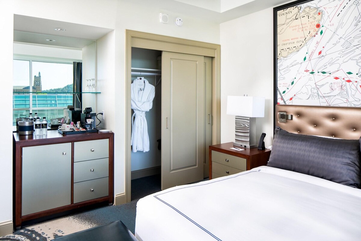 A hotel room with a bed, a dresser, a closet, a map on the wall, and a window with a view of a building.