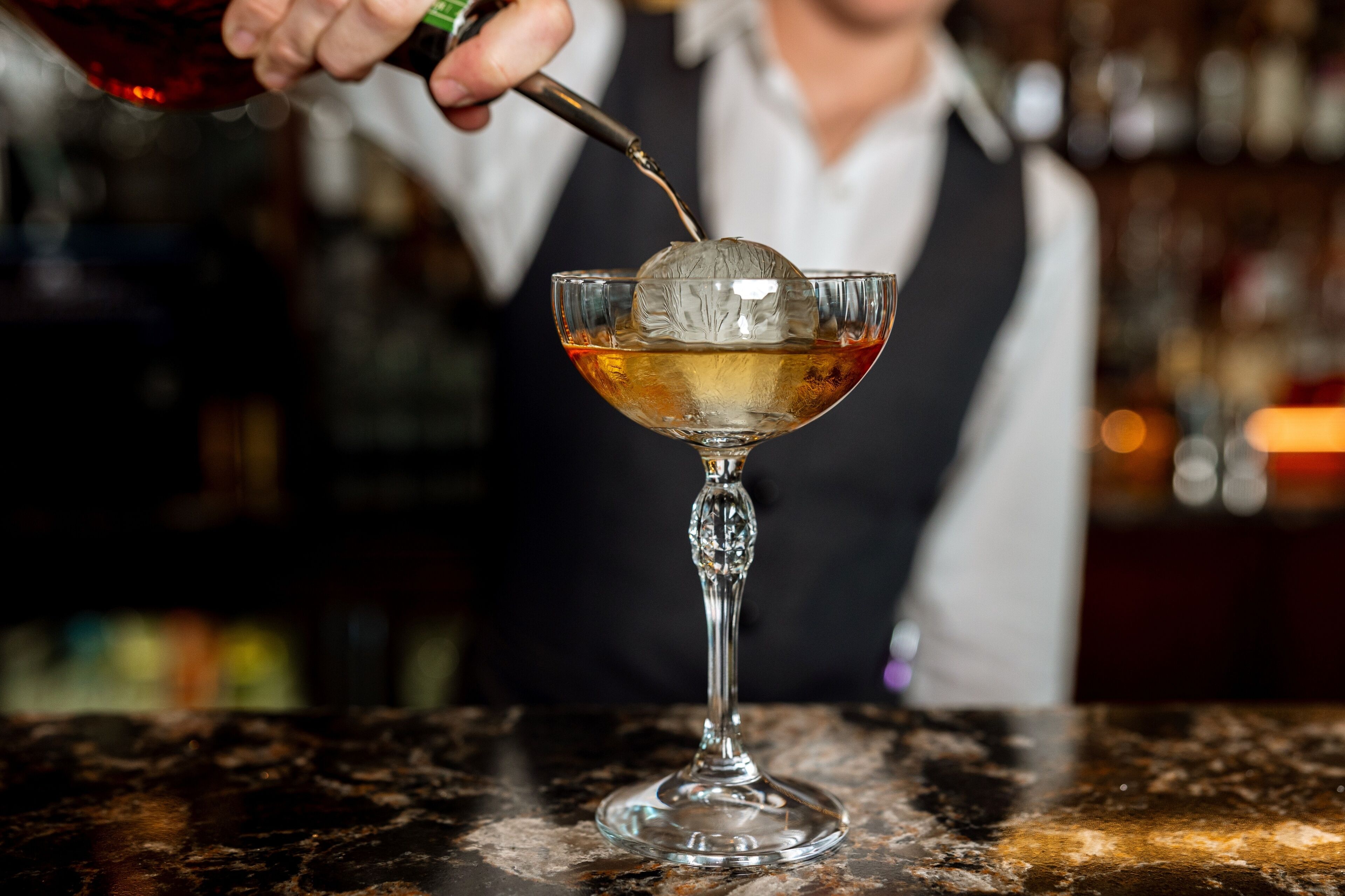A bartender pouring a drink into a glass with a decorative ice cube.