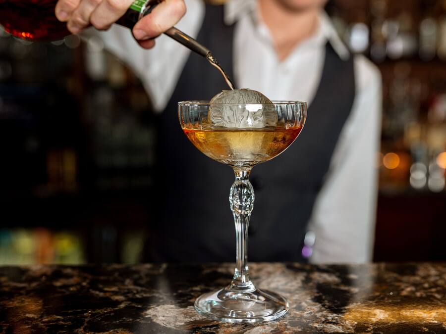 A bartender pouring a drink into a glass with a decorative ice cube.
