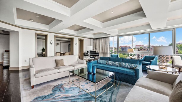 A spacious living room with a large window, a piano, and a sofa set.