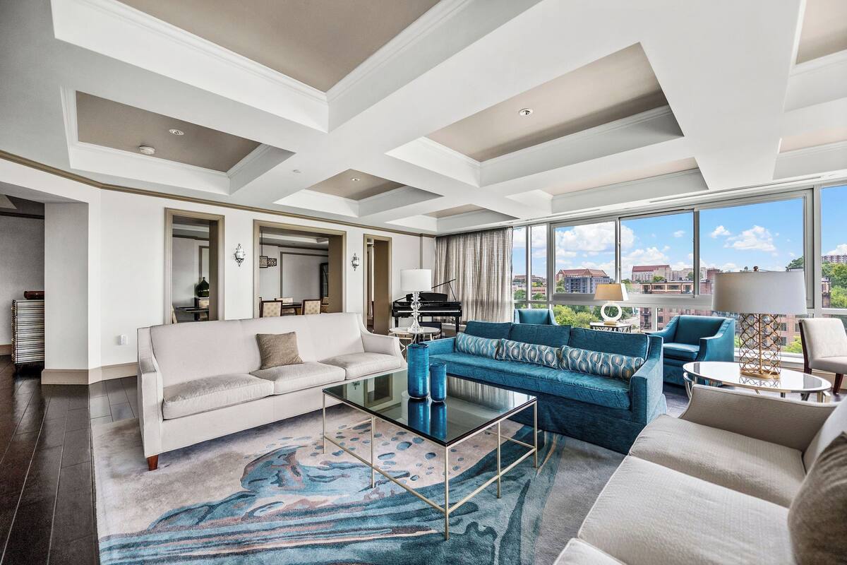 A spacious living room with a large window, a piano, and a sofa set.