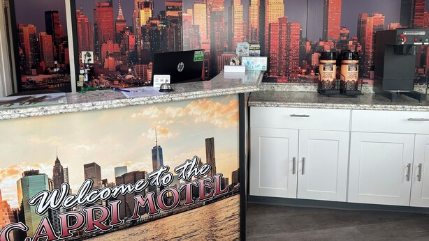 A hotel reception area with a cityscape mural, a laptop, and coffee dispensers. - Capri Motel By Belvilla Walla Walla US 12 (Walla Walla)