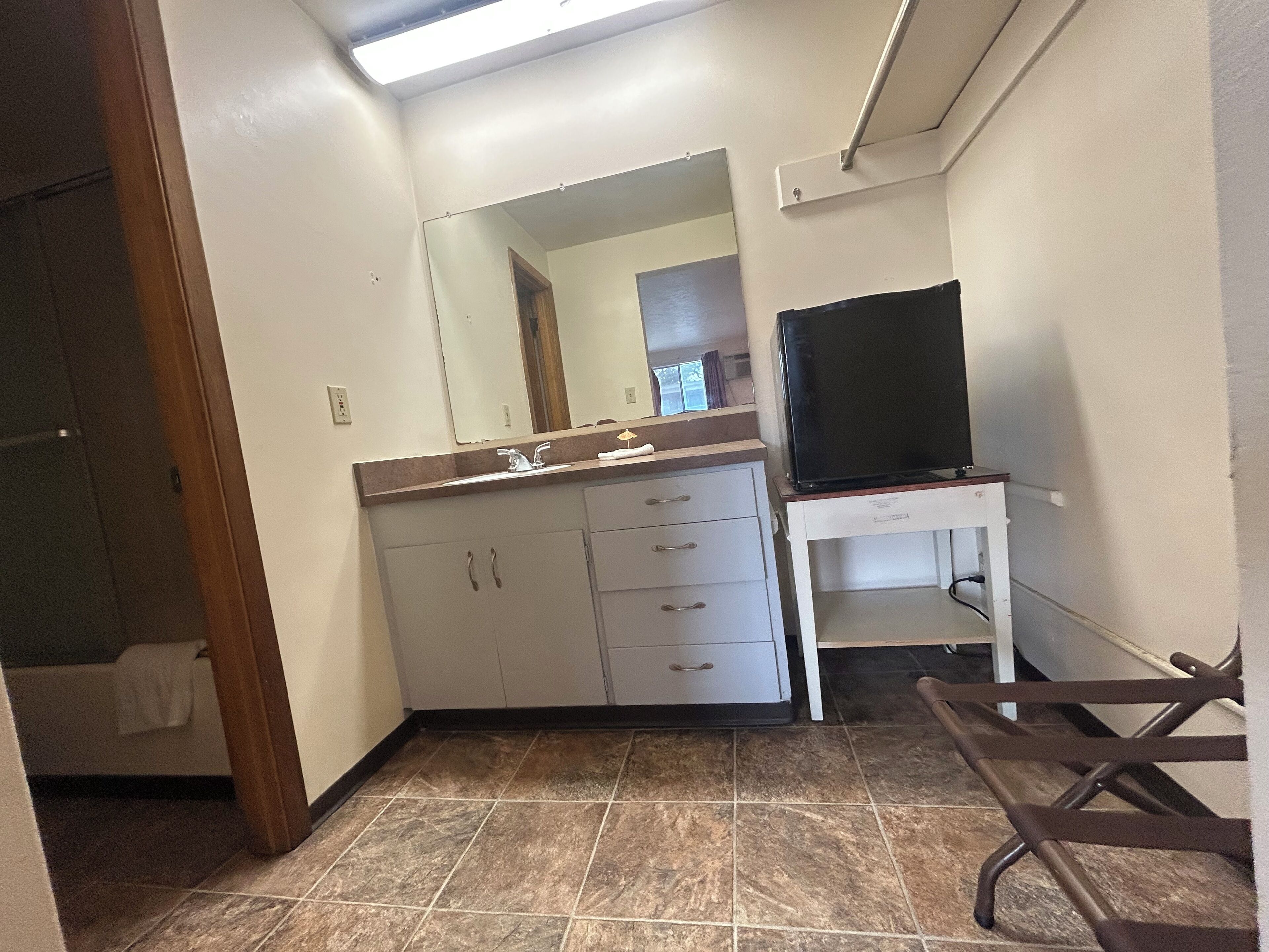 A bathroom with a sink, mirror, and a television on a stand.