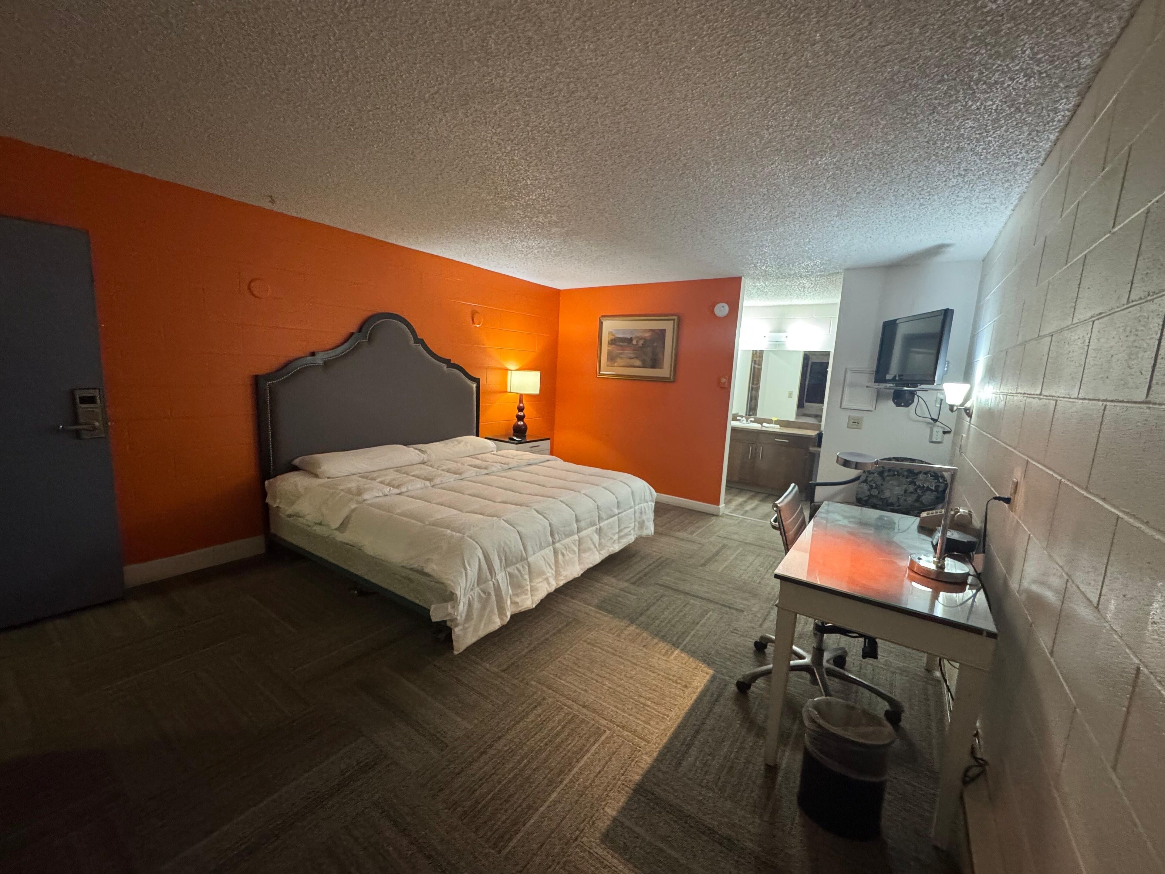 A hotel room with a bed, a desk with a chair, a lamp, and a television.