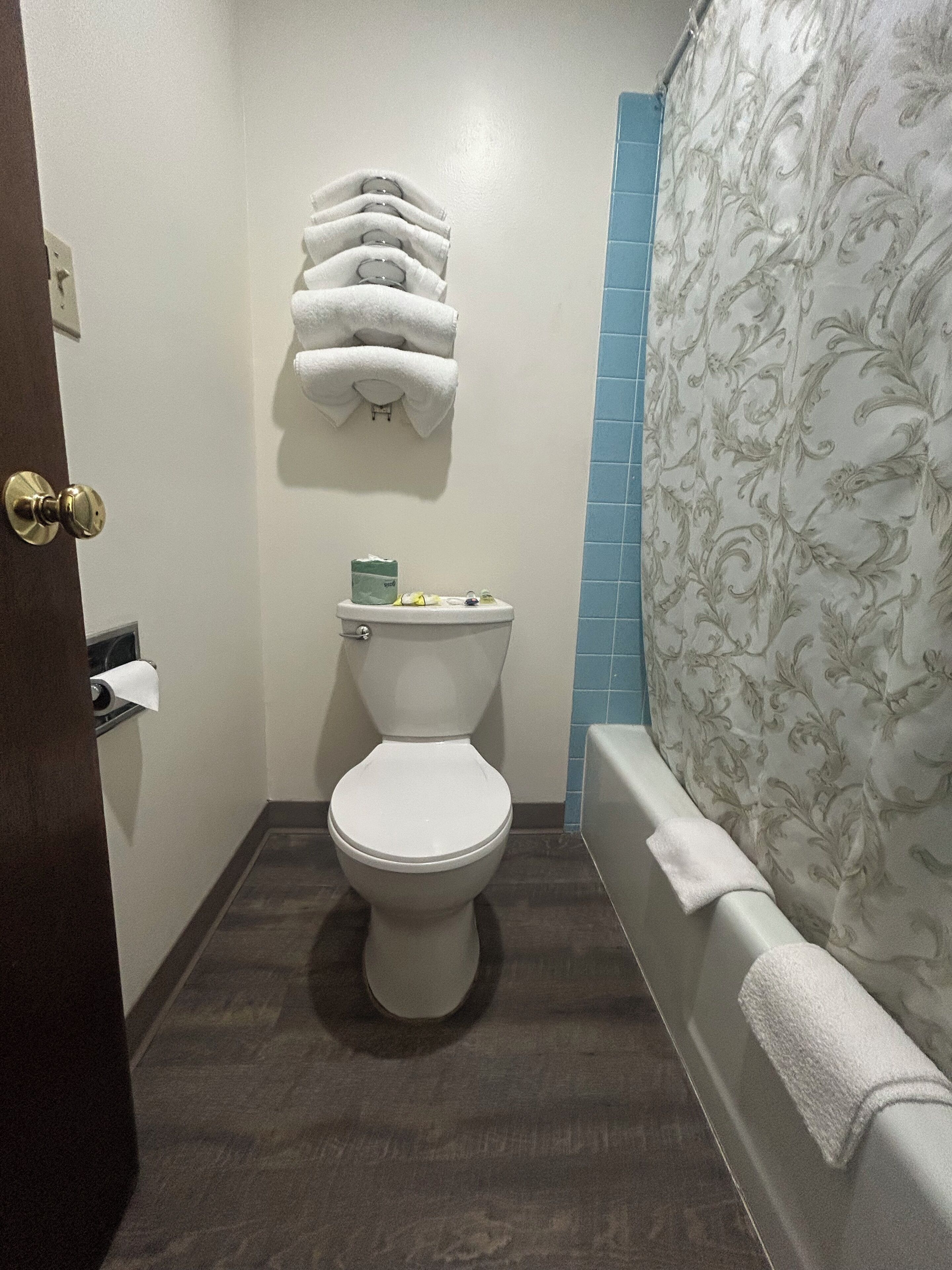 Un baño con inodoro, toallero con varias toallas, soporte para papel higiénico y cortina de ducha con estampado floral.
