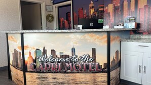 A reception desk at the Capri Motel with a cityscape mural, a sign indicating free Wi-Fi, and a HP computer. - Capri Motel By Belvilla Walla Walla US 12 (Walla Walla)