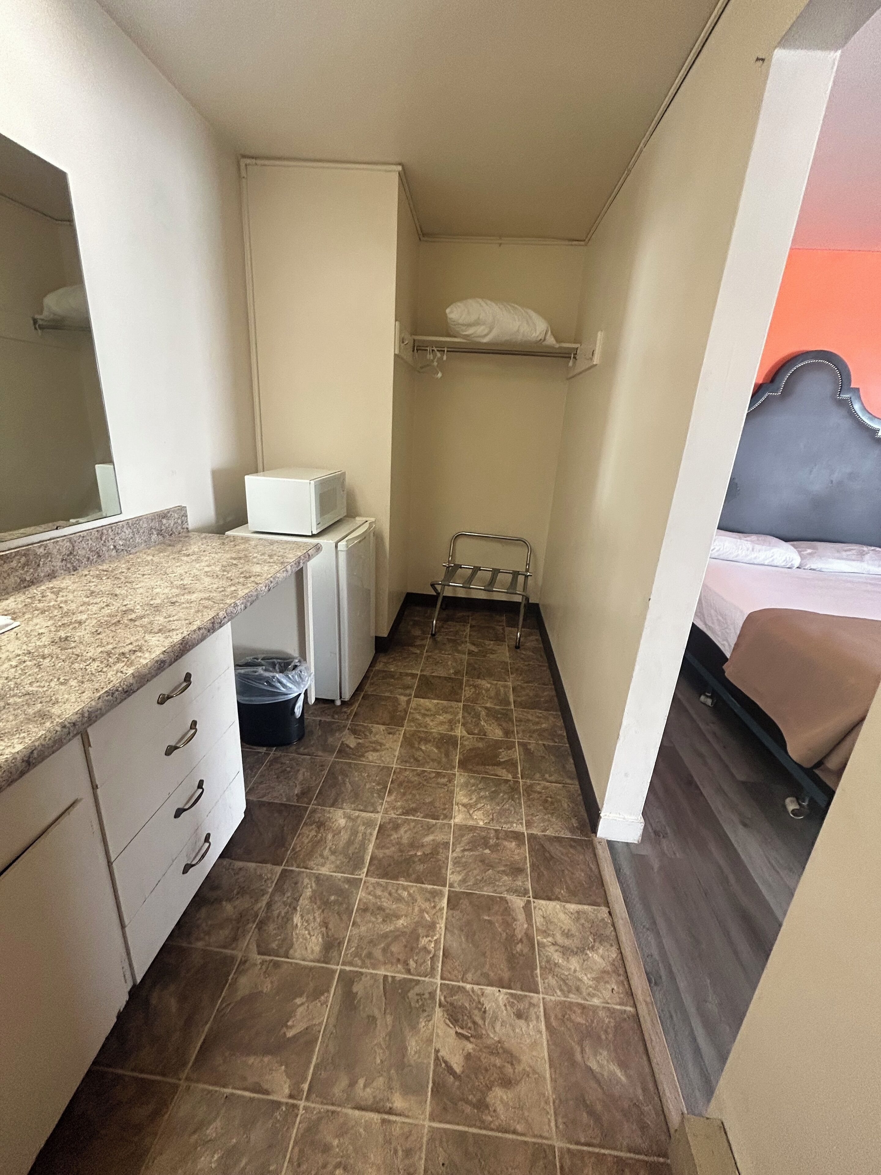 Una habitación compacta con kitchenette, una cama con cabecera y un pequeño rincón de descanso.