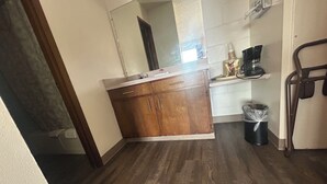 A small kitchen with wooden cabinets, a countertop, a coffee maker, and a trash can. - Capri Motel By Belvilla Walla Walla US 12 (Walla Walla)