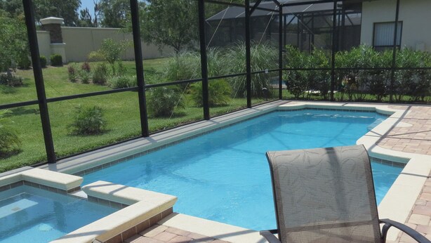 Une piscine dotée d’une enceinte en verre, entourée d’un patio aménagé avec des chaises et un petit jacuzzi.