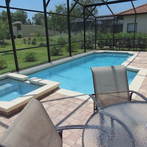 A swimming pool with a glass enclosure, surrounded by a patio area with chairs and a small hot tub.