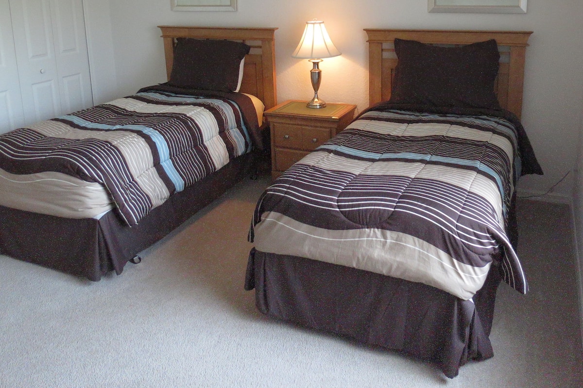Two single beds with striped bedding, a bedside table with a lamp, and two framed pictures on the wall.