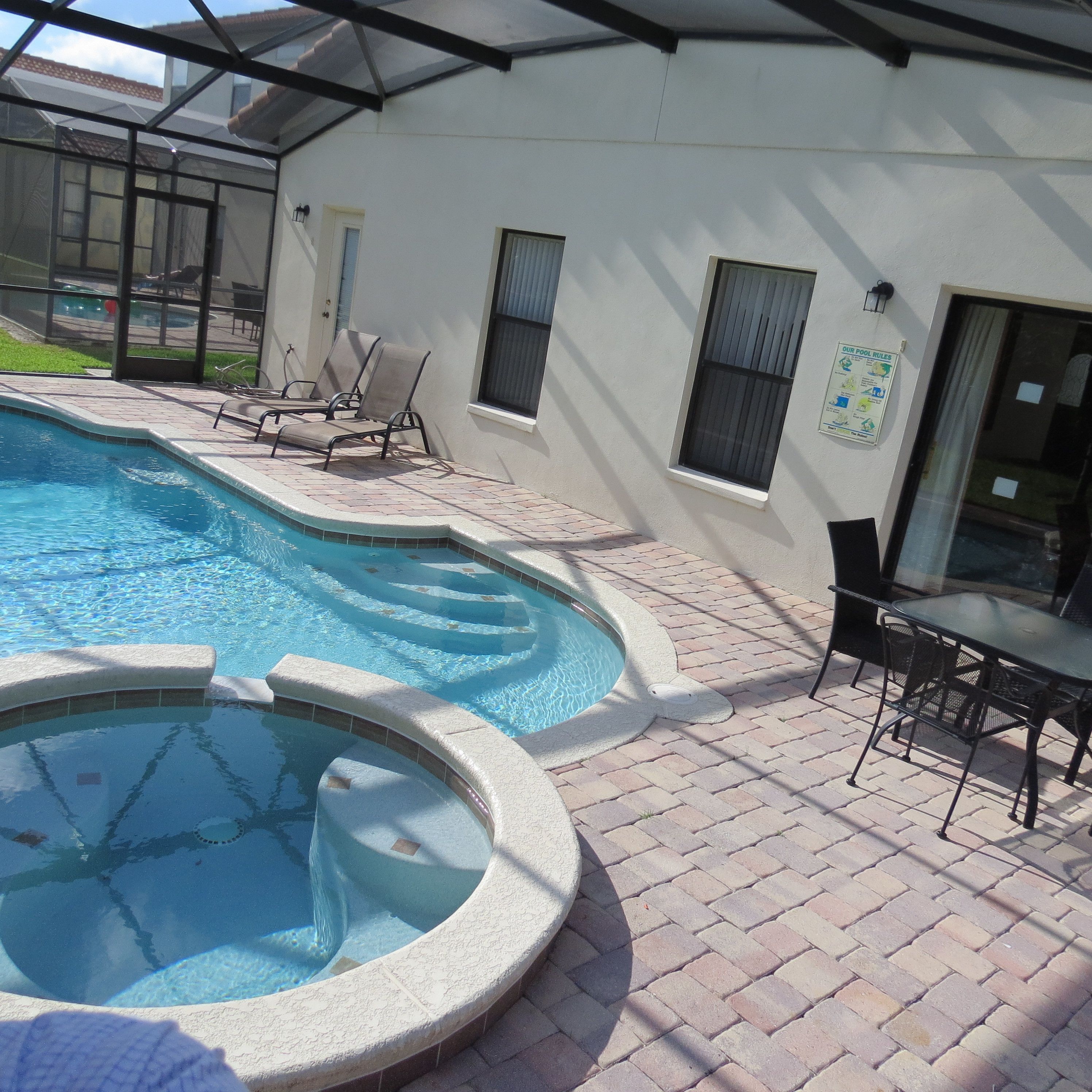 A swimming pool with a sunken section, surrounded by a brick patio, and adjacent to a building with windows and a door.