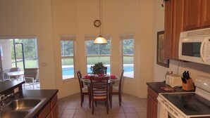 Une cuisine équipée d’une table à manger, de chaises, d’un four à micro-ondes, d’une cuisinière et offrant une vue sur une piscine.