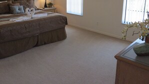 Une chambre à coucher avec un grand lit, une table de chevet, une lampe, un tableau encadré et une fenêtre avec des stores.
