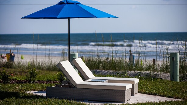 Une chaise longue installée sur la plage, avec un parasol bleu, d’où l’on a une vue sur l’océan.