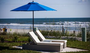 Une chaise longue installée sur la plage, avec un parasol bleu, d’où l’on a une vue sur l’océan.
