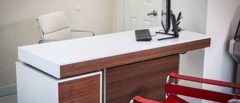 A modern office desk with a computer, a chair, and a red chair.