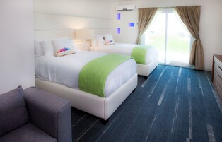 Habitación de hotel con dos camas, un sofá, un ventanal grande y piso alfombrado.