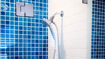 Une salle de bain avec des murs recouverts de carreaux bleus, un lavabo blanc et une douche équipée d’un pommeau de douche à main.