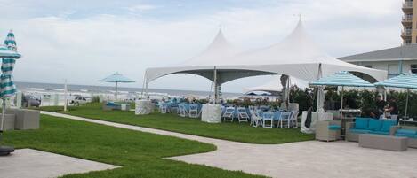 An outdoor event space with white tents, tables, and chairs, overlooking the ocean.