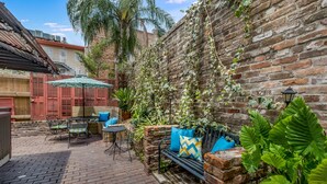 A patio area with a brick wall, a bench, a table with chairs, and an umbrella. - Royal Barracks Guest House (New Orleans)