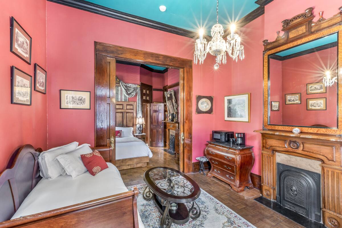 Um quarto com uma cama, cômoda de madeira, lareira e um candelabro.