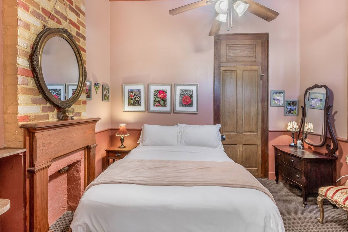 Um quarto com cama, cômoda, espelho e lareira.