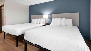 A hotel room with two beds, a nightstand with a lamp, and a door to the left.