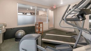 A fitness room with exercise equipment, a treadmill, a stationary bike, and a small wooden stool.