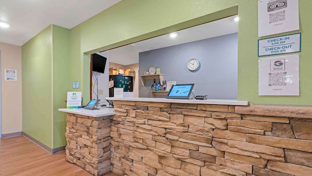 A reception area with a stone wall, a reception desk, a clock, and a digital screen.