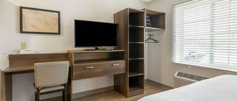 Habitación de hotel con escritorio de madera, silla, televisor, armario y cama.