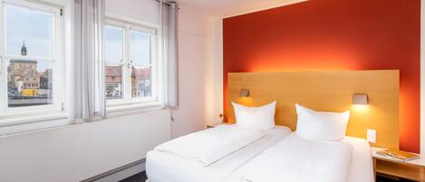 Habitación de hotel con dos camas, vista de edificios a través de la ventana y una pared de acento roja.