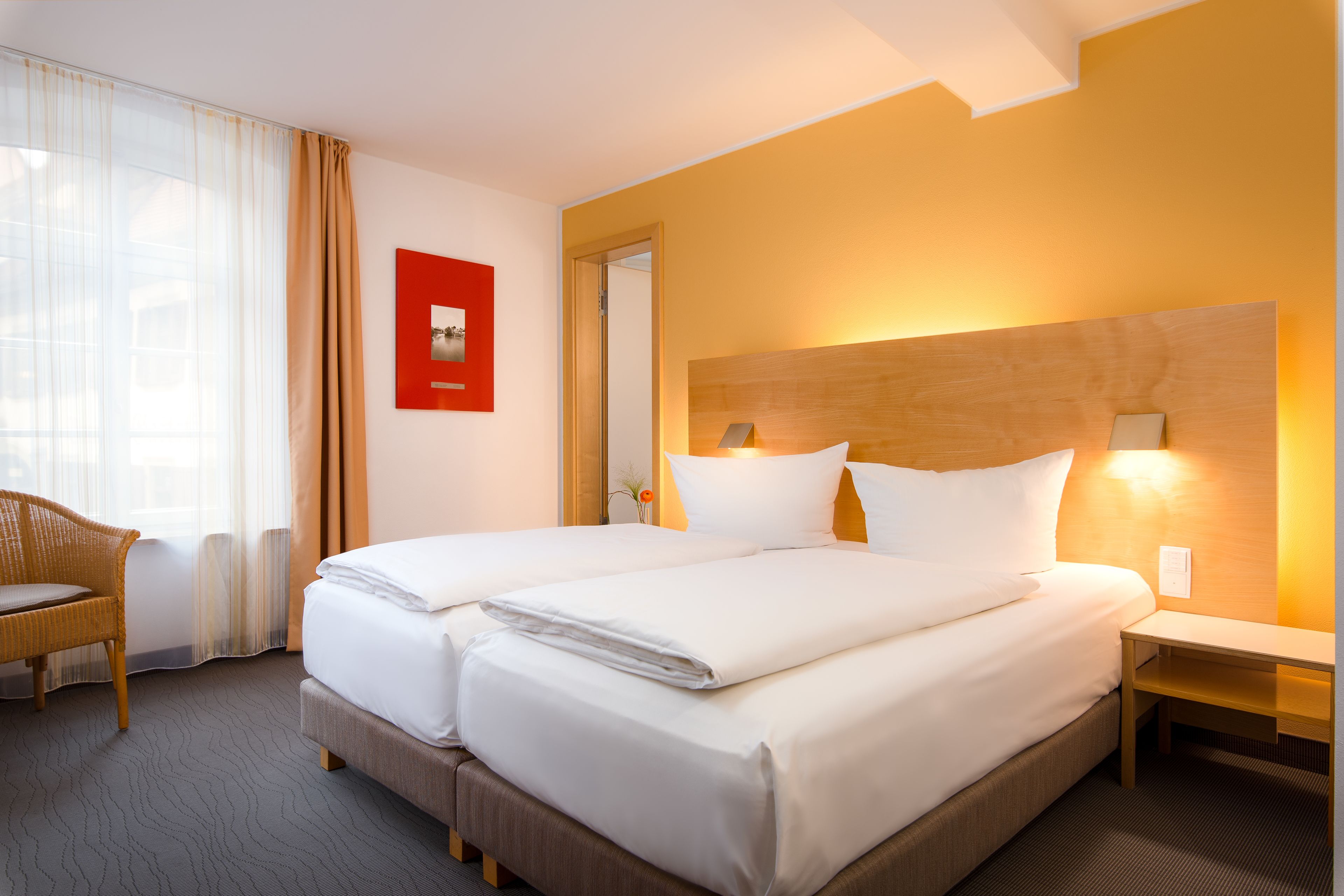 A hotel room with two beds, a wooden headboard, a nightstand, a chair, and a red picture on the wall.