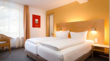 Habitación de hotel con dos camas, cabecero de madera, mesita de noche, una silla y un cuadro rojo en la pared.