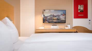 Quarto de hotel com uma cama, televisão sobre um console de madeira, luminária e quadro com moldura vermelha na parede.