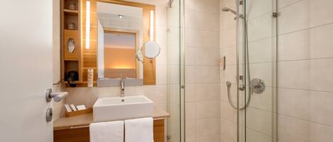 Un baño moderno con ducha envuelta en vidrio, lavamanos con espejo y tocador de madera.
