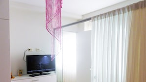 A room with a flat-screen TV on a white cabinet, a glass door leading to a balcony, and sheer curtains on the window. - Edificio California en Centro Histórico (Lima)