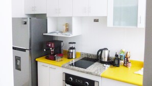 A compact kitchen with white cabinets, a stainless steel refrigerator, a coffee maker, a kettle, and a toaster. - Edificio California en Centro Histórico (Lima)