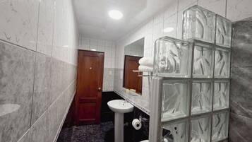 A bathroom with marble tiles, a wooden door, a white sink, a toilet, and a glass shower enclosure.