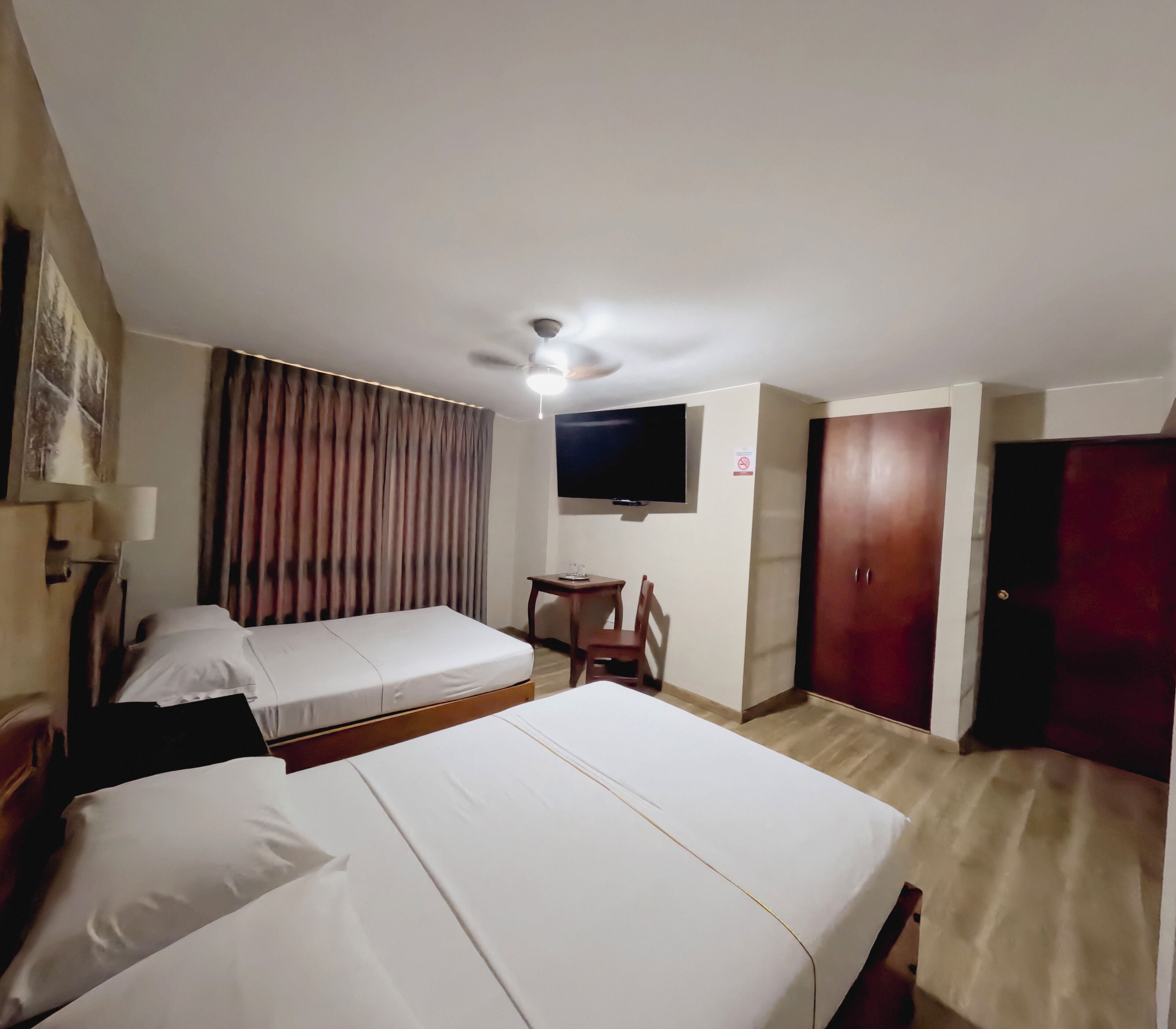 A hotel room with two beds, a desk, a chair, a television, and a wardrobe.