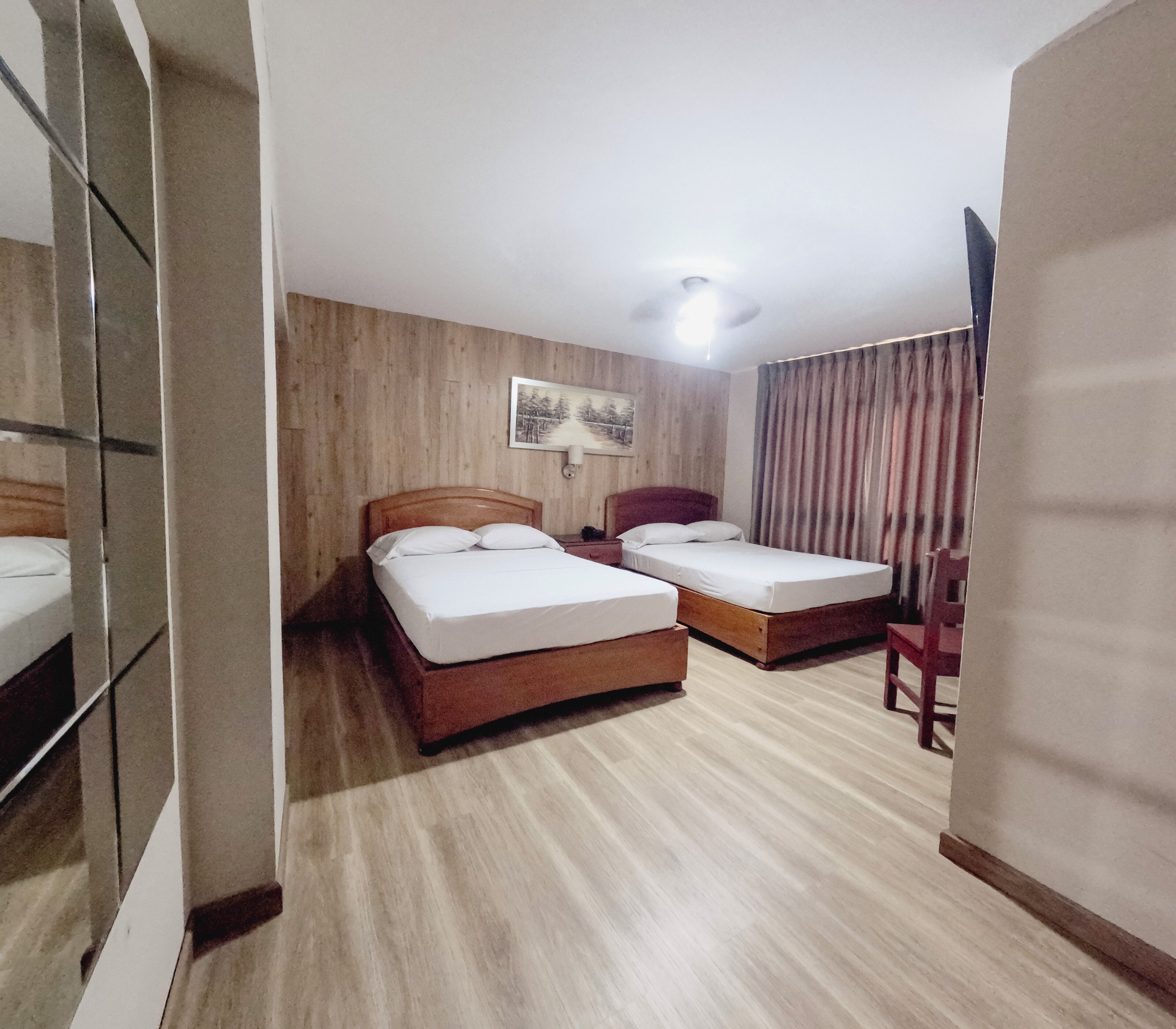 A hotel room with two beds, a wooden floor, a painting on the wall, and a window with curtains.
