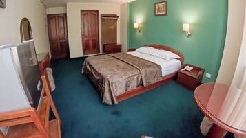 Una habitación de hotel con cama, mesita de noche, lámpara y escritorio con silla.