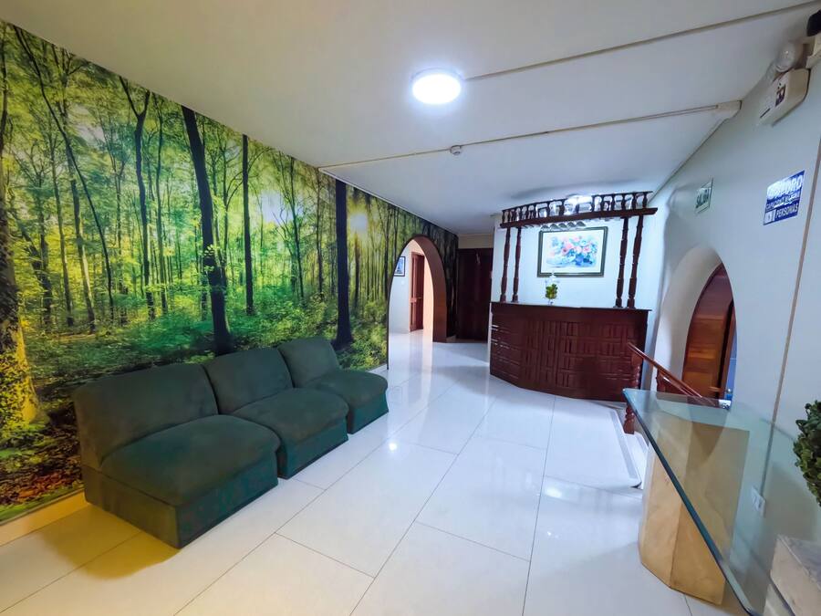 Un área de recepción con un sofá verde, un mostrador de madera y un mural con motivos forestales en la pared.