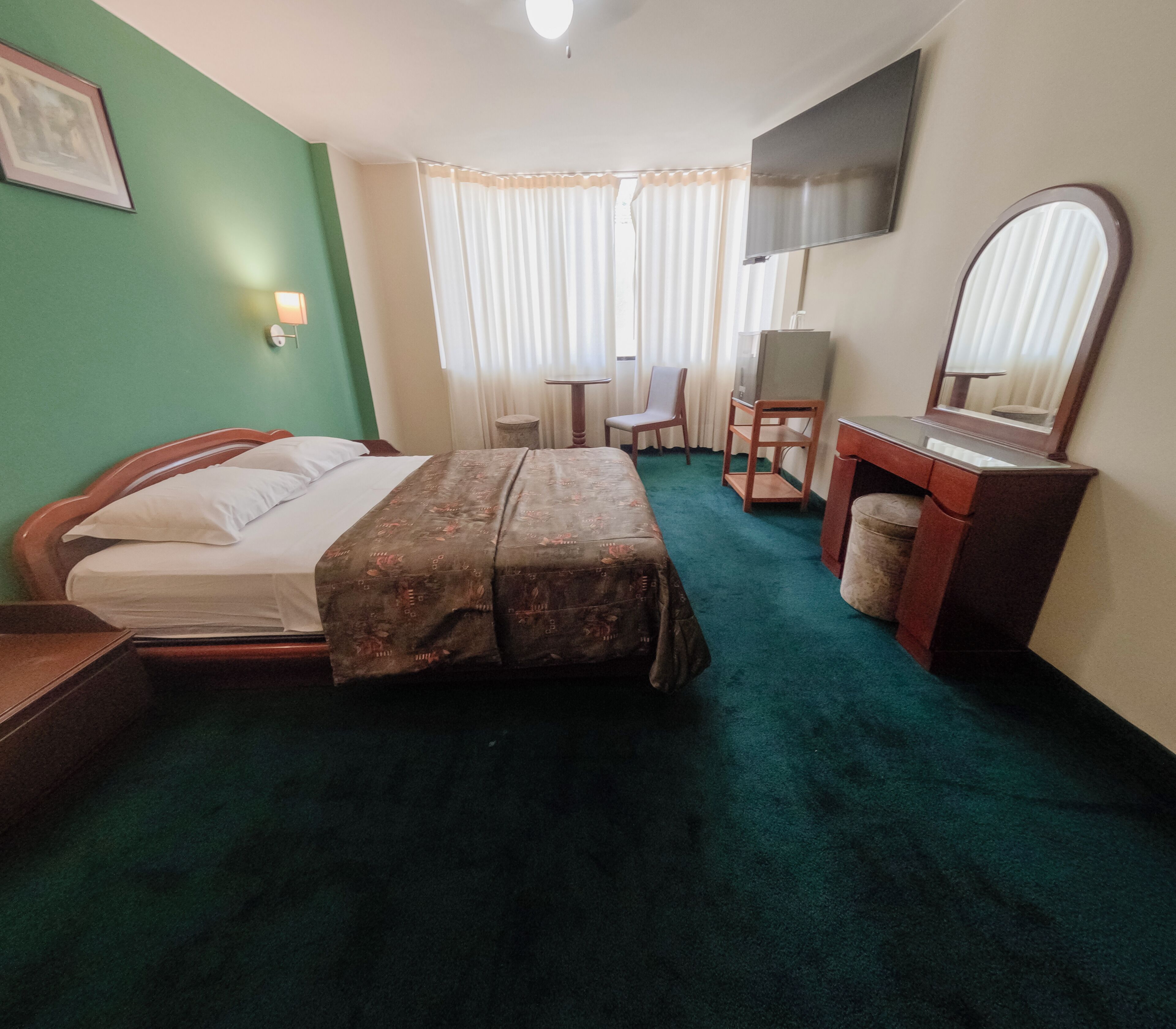 A hotel room with a bed, a desk, a chair, a television, and a mirror.