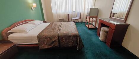 A hotel room with a bed, a desk, a chair, a television, and a mirror.